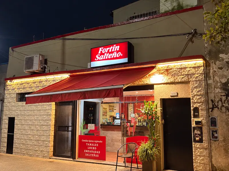 Frente iluminado de Fortín Salteño en Florida, de noche, con su cartel rojo y el toldo bordó